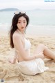 A woman in a white bikini sitting on the beach.