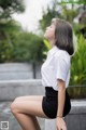 A woman in a white shirt and black skirt sitting on a ledge.