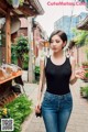 A woman in a black tank top and jeans walking down a street.