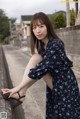 A woman in a blue dress leaning against a wall.